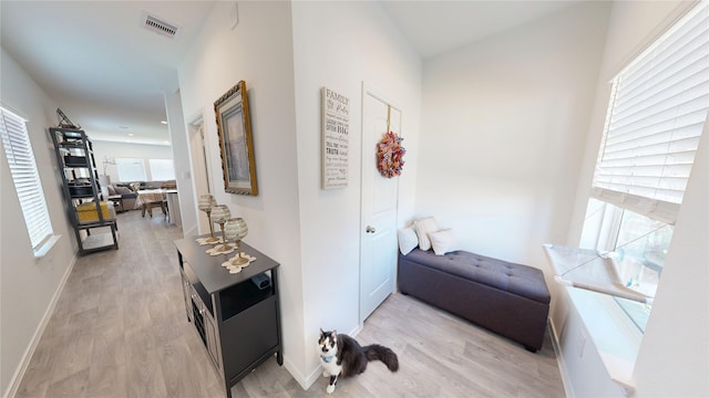 hallway featuring visible vents, light wood-style flooring, and baseboards