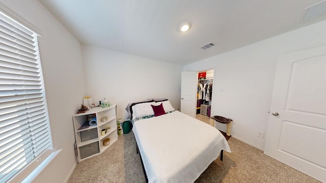 bedroom featuring light colored carpet, a walk in closet, and visible vents