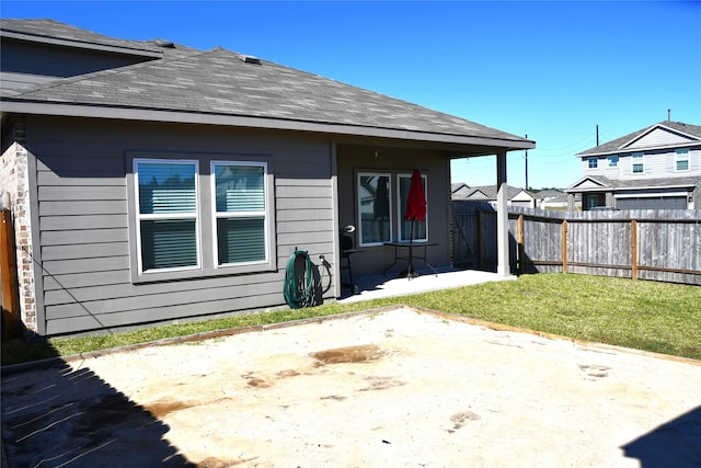 back of property with a yard, roof with shingles, a patio area, and fence