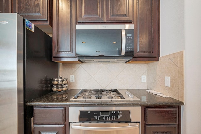 kitchen with appliances with stainless steel finishes, dark stone countertops, dark brown cabinets, and tasteful backsplash