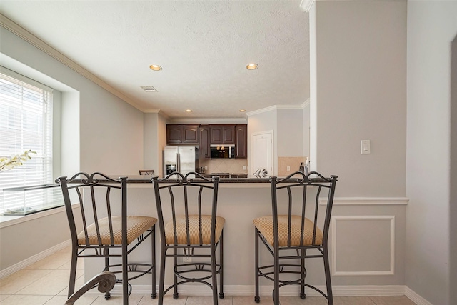 kitchen featuring stainless steel appliances, dark brown cabinets, dark countertops, and a kitchen bar