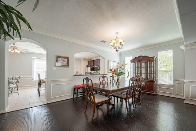 dining room with a textured ceiling, arched walkways, a decorative wall, and wood finished floors