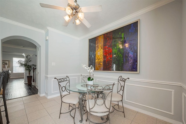 dining space with arched walkways, crown molding, wainscoting, a textured ceiling, and tile patterned floors