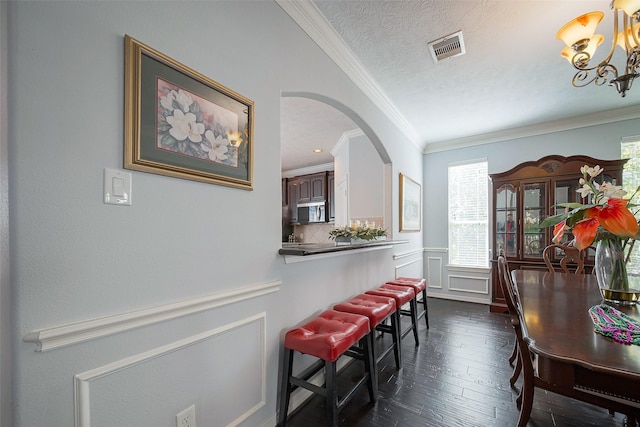 dining space featuring a textured ceiling, a decorative wall, dark wood-style flooring, visible vents, and ornamental molding