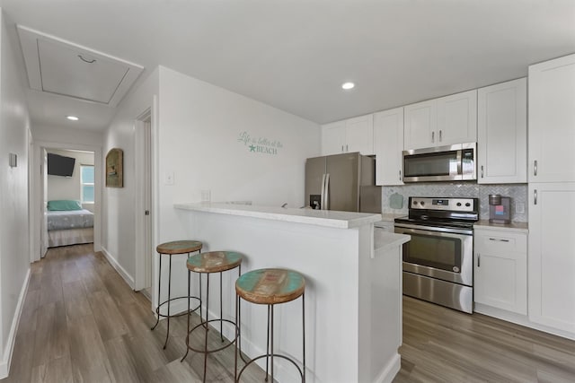 kitchen featuring tasteful backsplash, white cabinets, a breakfast bar, wood finished floors, and stainless steel appliances