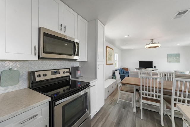 kitchen with wood finished floors, visible vents, white cabinets, appliances with stainless steel finishes, and backsplash