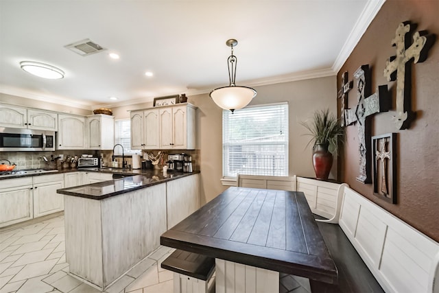 kitchen with dark countertops, stainless steel microwave, visible vents, crown molding, and a peninsula