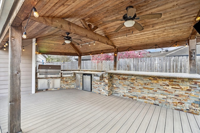 wooden terrace featuring fence, an outdoor kitchen, ceiling fan, a gazebo, and grilling area