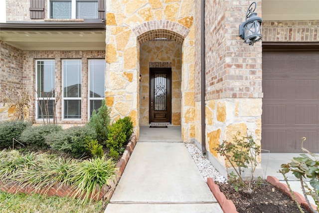 entrance to property featuring a garage, stone siding, and brick siding