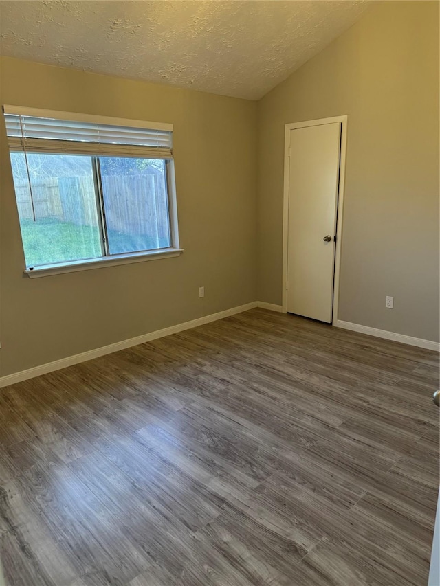 spare room featuring a textured ceiling, baseboards, vaulted ceiling, and wood finished floors