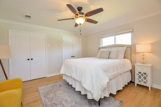 bedroom with light wood finished floors, baseboards, multiple closets, and ornamental molding