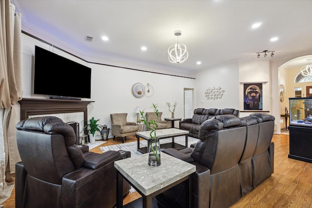 living area with ornamental molding, a tiled fireplace, arched walkways, light wood-style floors, and a chandelier