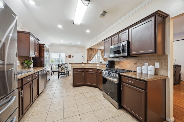 kitchen with visible vents, a peninsula, ornamental molding, stainless steel appliances, and tasteful backsplash