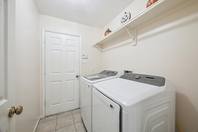 washroom with light tile patterned floors, laundry area, washing machine and dryer, and a textured ceiling