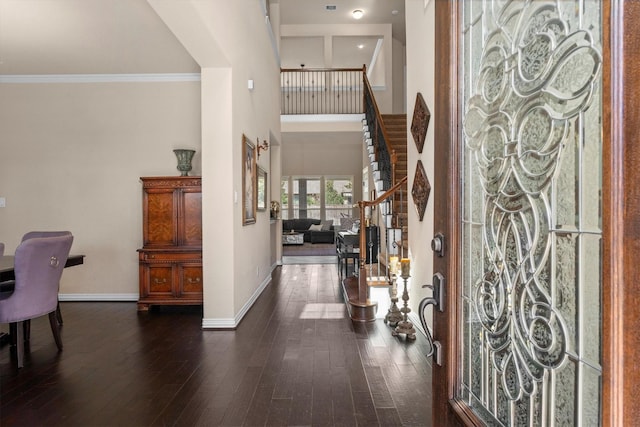 entryway featuring baseboards, a towering ceiling, dark wood-type flooring, stairs, and crown molding