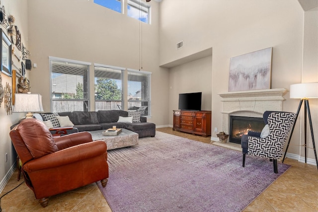 living room featuring a towering ceiling, visible vents, baseboards, tile patterned floors, and a glass covered fireplace