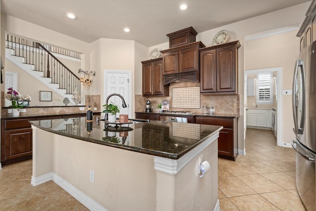 kitchen with light tile patterned floors, a kitchen island with sink, a sink, backsplash, and freestanding refrigerator