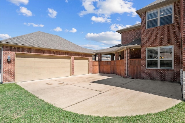 view of side of property featuring concrete driveway, brick siding, an attached garage, and roof with shingles