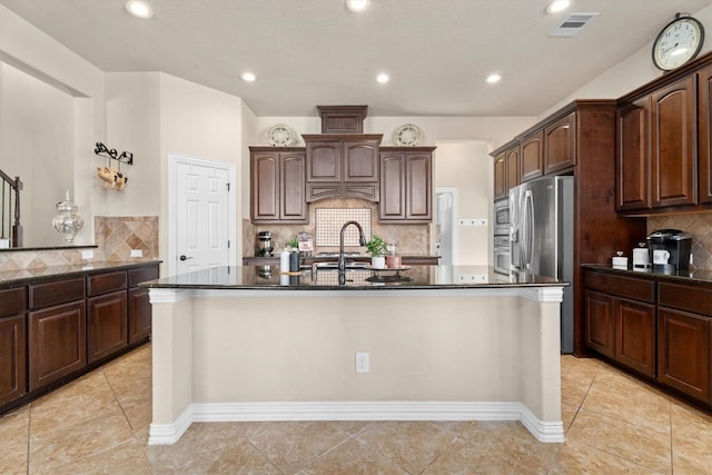 kitchen with dark brown cabinets, appliances with stainless steel finishes, an island with sink, and visible vents