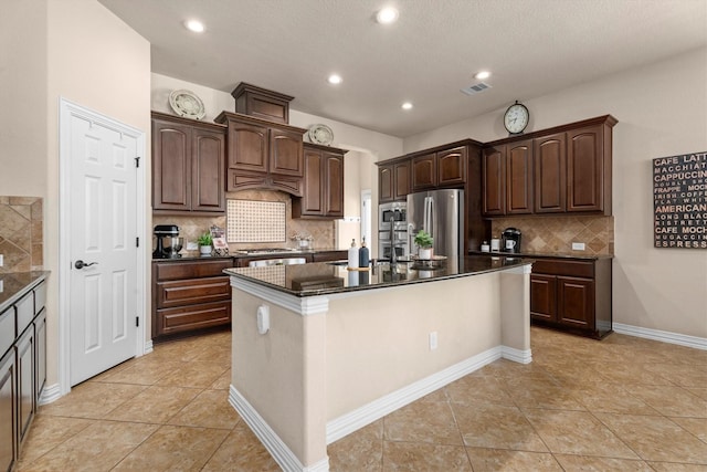 kitchen featuring light tile patterned floors, stainless steel appliances, visible vents, dark brown cabinets, and an island with sink