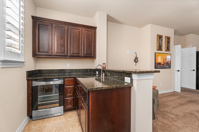 kitchen featuring wine cooler, a peninsula, a sink, dark brown cabinets, and dark stone counters