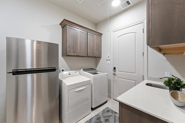 clothes washing area with light tile patterned floors, washing machine and dryer, a sink, visible vents, and cabinet space