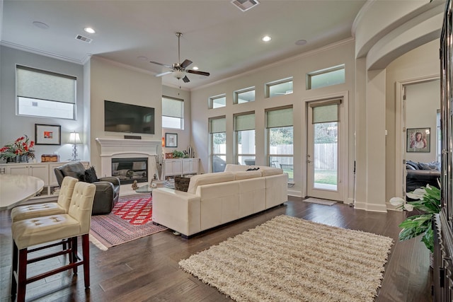 living area with crown molding, visible vents, dark wood-style flooring, and a glass covered fireplace