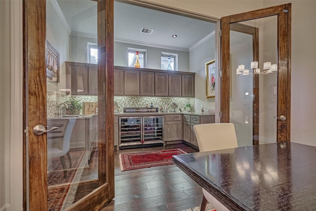 bar with dark wood-style flooring, tasteful backsplash, visible vents, ornamental molding, and beverage cooler