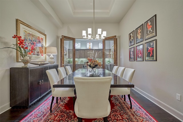 dining room with dark wood-type flooring, a raised ceiling, a notable chandelier, and baseboards