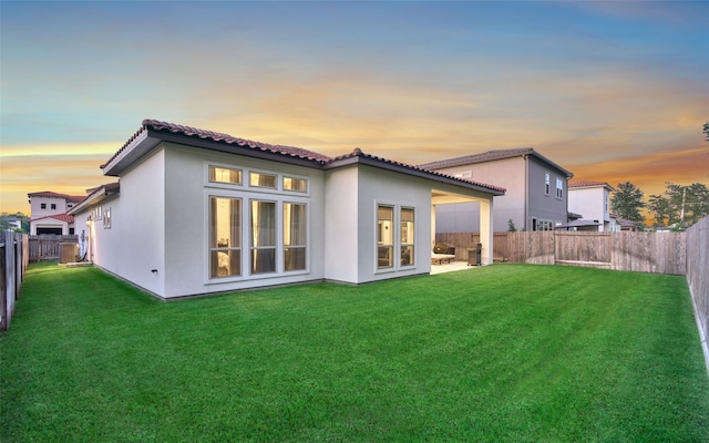 back of house featuring a yard, a tile roof, a fenced backyard, and stucco siding