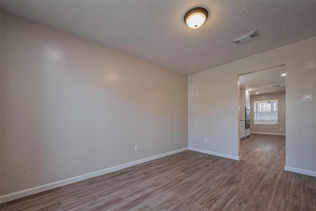 unfurnished room with baseboards, a textured ceiling, visible vents, and wood finished floors