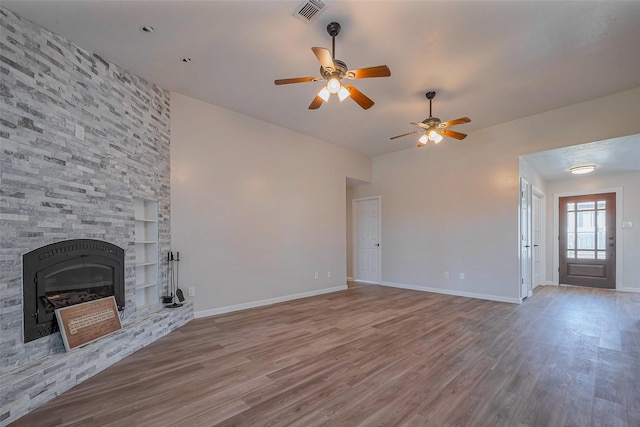 unfurnished living room featuring baseboards, visible vents, wood finished floors, and a stone fireplace