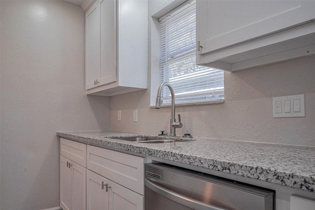 kitchen featuring a textured wall, stainless steel dishwasher, white cabinets, a sink, and light stone countertops