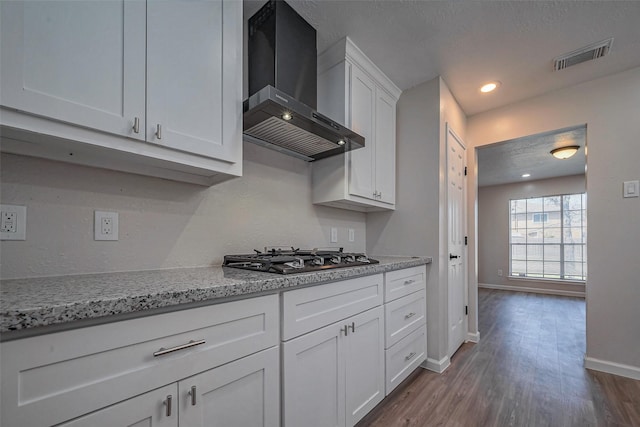 kitchen with baseboards, visible vents, white cabinets, wall chimney range hood, and stainless steel gas stovetop