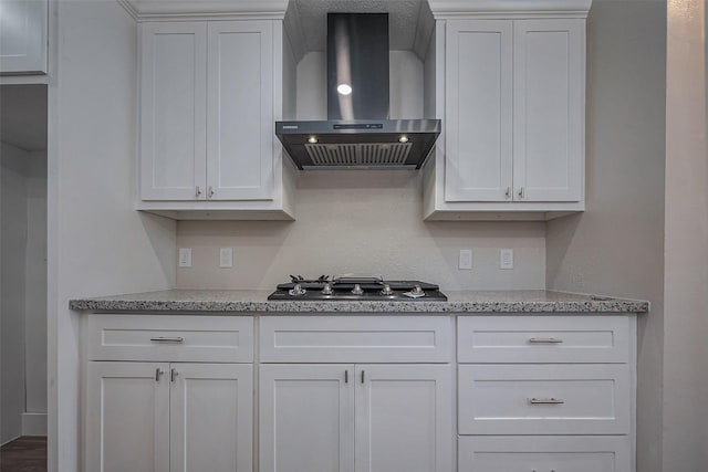 kitchen with wall chimney exhaust hood, white cabinetry, light stone countertops, and stainless steel gas stovetop