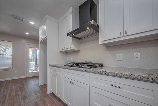 kitchen featuring stainless steel gas cooktop, visible vents, dark wood-type flooring, white cabinetry, and wall chimney range hood