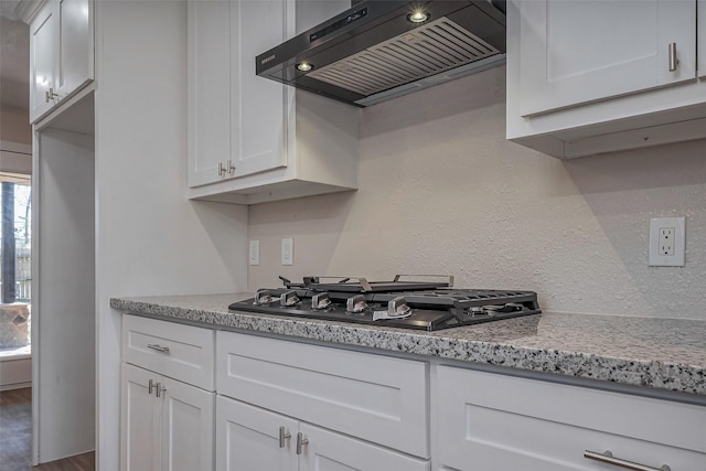 kitchen featuring stainless steel gas cooktop, light stone counters, white cabinetry, and range hood