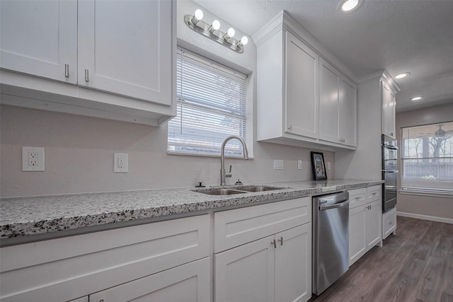 kitchen with light stone counters, dark wood-type flooring, white cabinets, a sink, and dishwasher