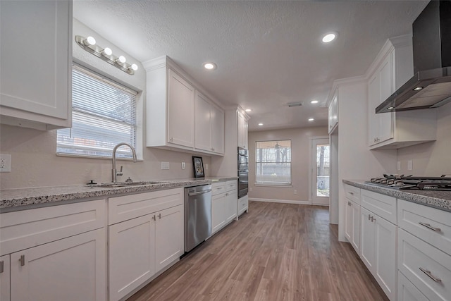 kitchen with appliances with stainless steel finishes, white cabinetry, a sink, and wall chimney exhaust hood