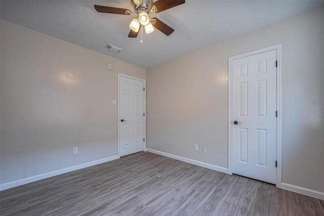 empty room featuring a ceiling fan, visible vents, baseboards, and wood finished floors