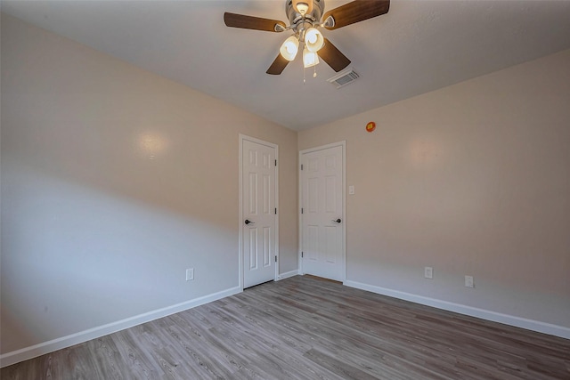 empty room with a ceiling fan, wood finished floors, visible vents, and baseboards