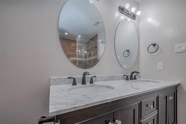 bathroom featuring double vanity, tiled shower, a sink, and visible vents