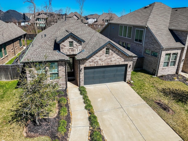 french country style house featuring fence, concrete driveway, an attached garage, a shingled roof, and brick siding