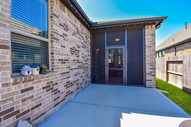 entrance to property featuring a patio, brick siding, and fence