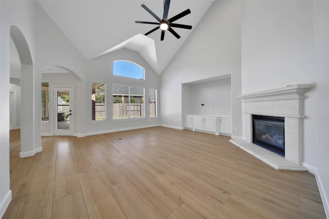 unfurnished living room featuring high vaulted ceiling, a ceiling fan, baseboards, light wood-style floors, and a glass covered fireplace