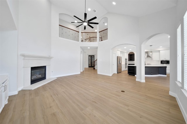 unfurnished living room with visible vents, stairway, a glass covered fireplace, ceiling fan, and light wood-type flooring