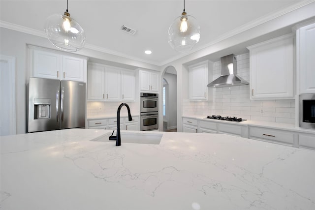 kitchen featuring arched walkways, stainless steel appliances, a sink, visible vents, and wall chimney range hood