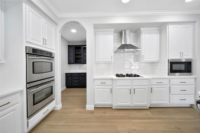 kitchen with gas stovetop, light wood-style flooring, double oven, built in microwave, and wall chimney exhaust hood