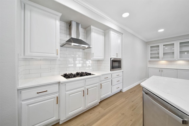 kitchen with stainless steel appliances, white cabinetry, wall chimney range hood, light wood finished floors, and crown molding