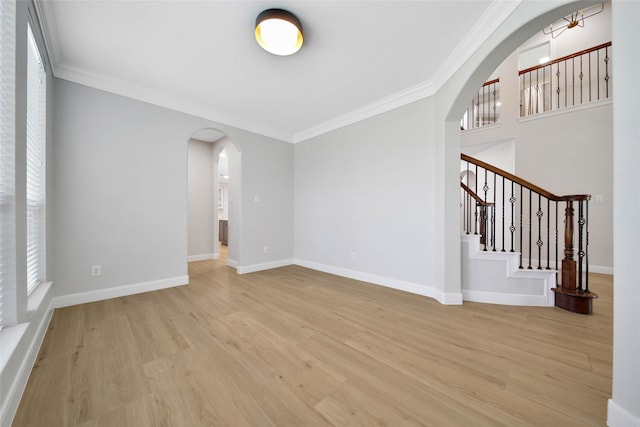 empty room with arched walkways, light wood finished floors, and ornamental molding